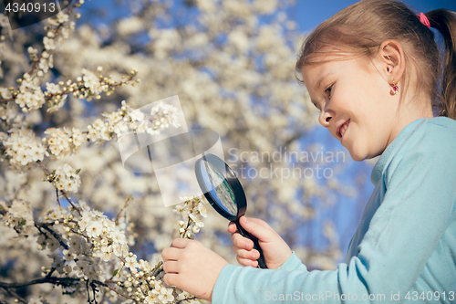 Image of Happy little girl exploring nature with magnifying glass at the 