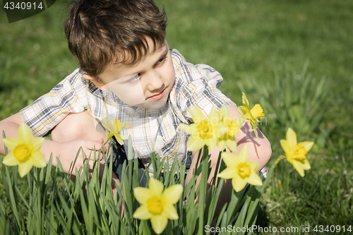 Image of One little boy sitting in the grass at the day time. 