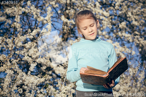 Image of One little girl reading a book on a blossom tree.