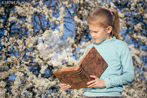 Image of One little girl reading a book on a blossom tree.