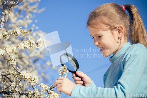 Image of Happy little girl exploring nature with magnifying glass at the 