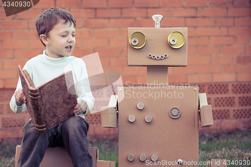 Image of One little boy reading to  robot from cardboard boxes outdoors.