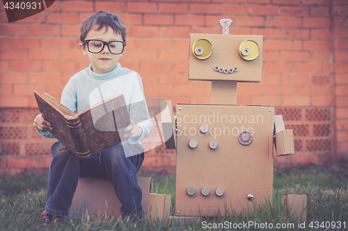 Image of One little boy reading to  robot from cardboard boxes outdoors.