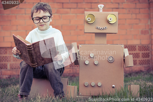 Image of One little boy reading to  robot from cardboard boxes outdoors.