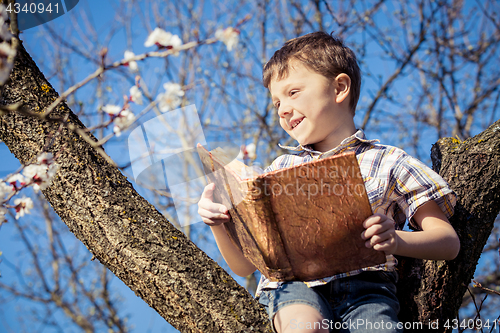 Image of One little boy reading a book on a blossom tree.