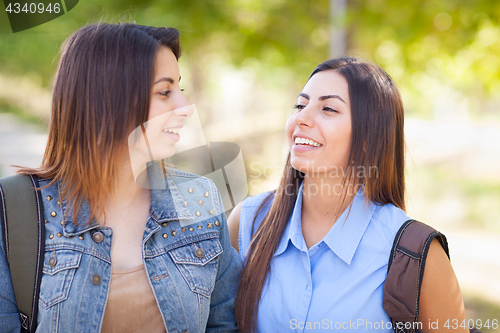 Image of Two Beautiful Young Ethnic Twin Sisters With Backpacks Walking O