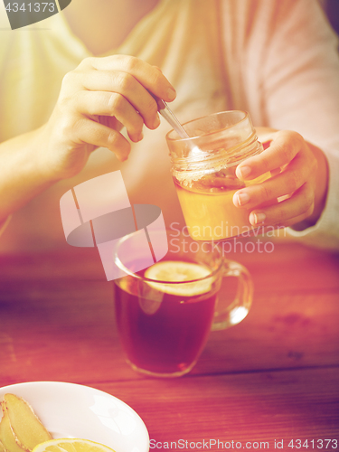 Image of close up of woman adding honey to tea with lemon