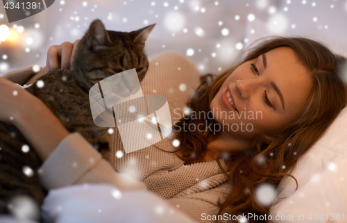 Image of happy young woman with cat lying in bed at home
