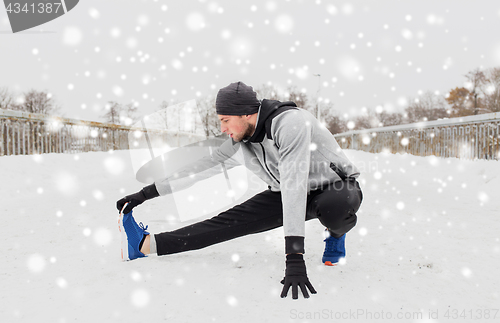 Image of man exercising and stretching leg on winter bridge