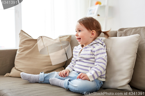 Image of happy smiling baby girl sitting on sofa at home