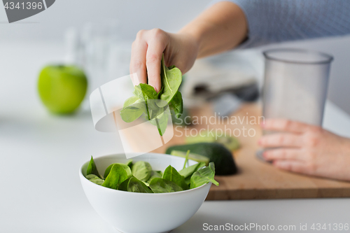 Image of close up of woman hand adding spinach to bowl