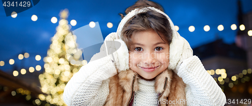 Image of happy girl wearing earmuffs over christmas lights