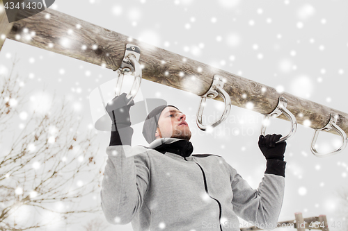 Image of young man exercising on horizontal bar in winter