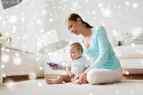 Image of happy mother showing smartphone to baby at home