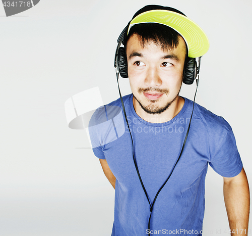 Image of young asian man in hat and headphones listening music on white b