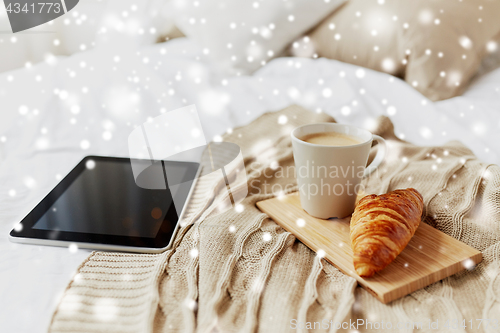 Image of tablet pc, coffee and croissant on bed at home