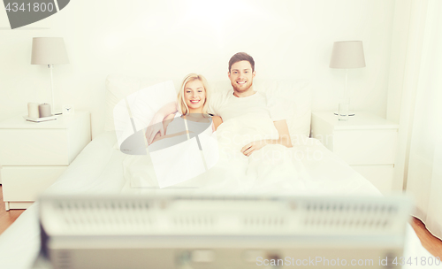 Image of happy couple lying in bed at home and watching tv