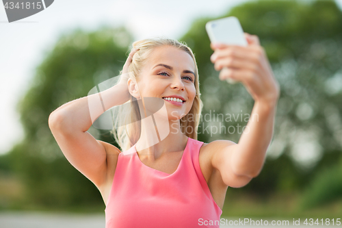 Image of happy woman taking selfie with smartphone outdoors