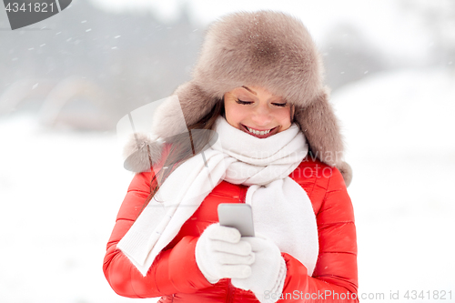 Image of happy woman in winter fur hat with smartphone