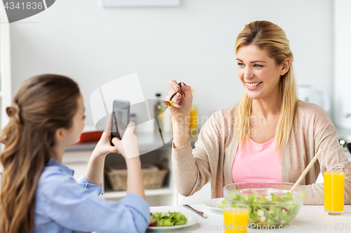 Image of girl photographing mother by smartphone at home