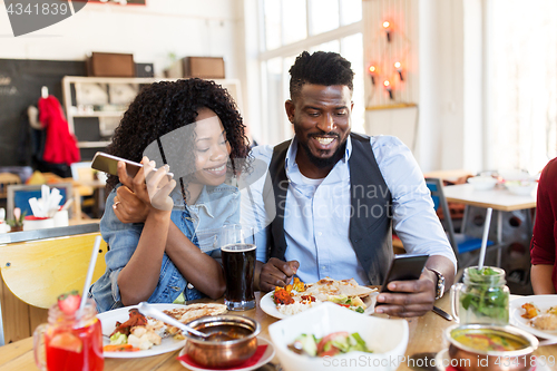 Image of happy man and woman with smartphones at restaurant