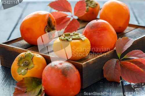 Image of Orange persimmon and autumn leaves on wooden box.
