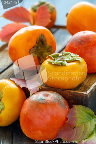 Image of Orange persimmon and autumn leaves on wooden box.