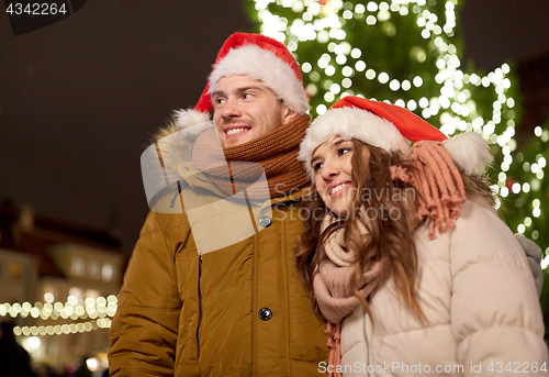 Image of happy couple in santa hats at christmas tree