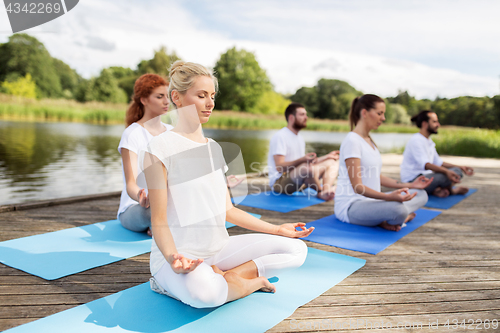 Image of people meditating in yoga lotus pose outdoors