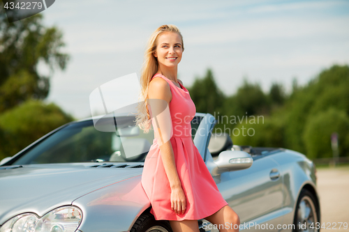 Image of happy young woman posing at convertible car