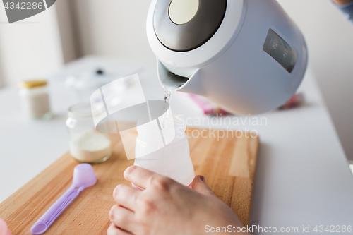 Image of hands with kettle and bottle making baby milk