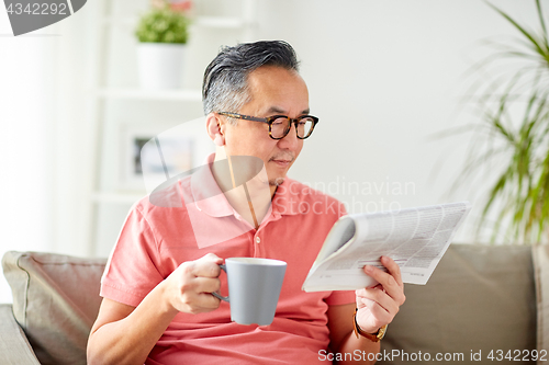 Image of man drinking coffee and reading newspaper at home