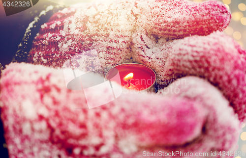 Image of close up of hands in winter mittens holding candle