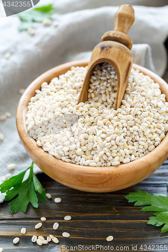 Image of Wooden scoop in bowl with dry pearl barley.