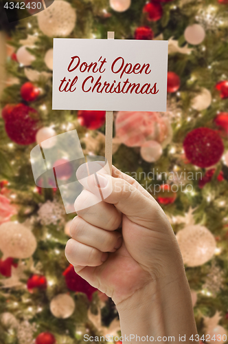 Image of Hand Holding Don\'t Open Til Christmas Card In Front of Decorated