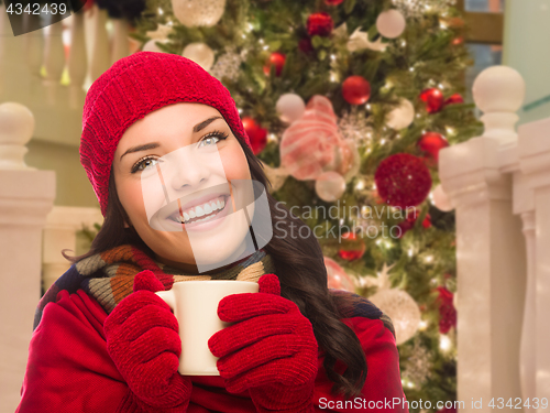 Image of Warmly Dressed Female With Mug In Front of Decorated Christmas T