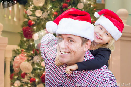 Image of Father and Daughter Wearing Santa Hats In Front of Decorated Chr