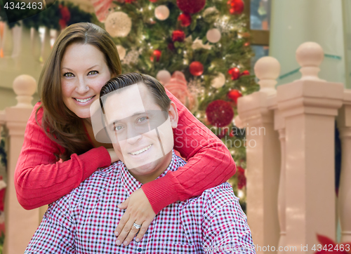 Image of Caucasian Couple Hugging In Front of Decorated Christmas Tree.