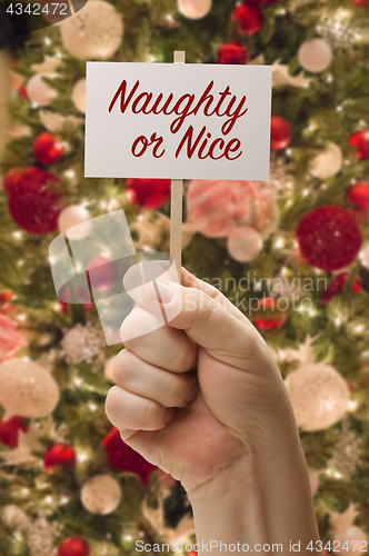 Image of Hand Holding Naughty of Nice Card In Front of Decorated Christma