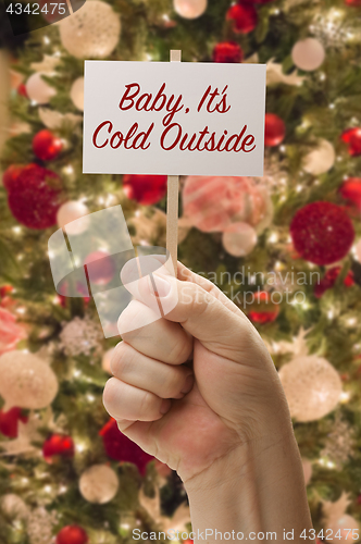 Image of Hand Holding Baby, It\'s Cold Outside Card In Front of Decorated 