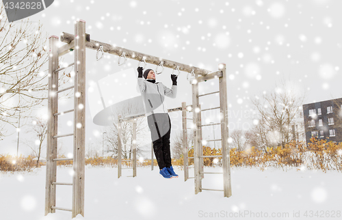 Image of young man exercising on horizontal bar in winter