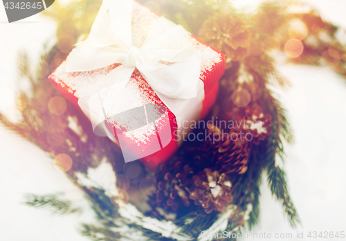 Image of close up of christmas gift and fir wreath on snow