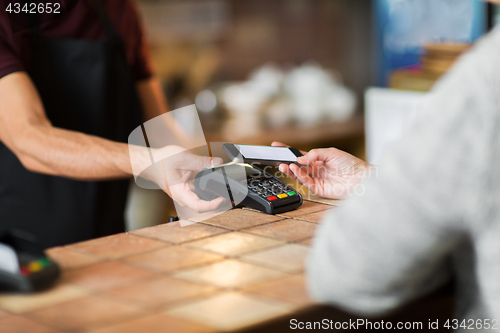 Image of hands with payment terminal and smartphone at bar