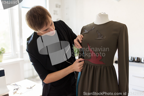 Image of fashion designer with dummy making dress at studio