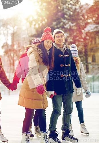 Image of happy friends ice skating on rink outdoors