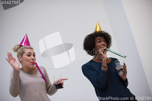 Image of smiling women in party caps blowing to whistles