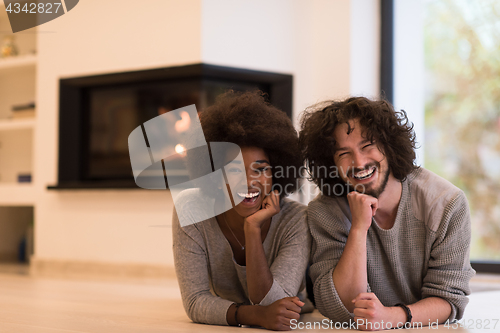 Image of multiethnic couple lying on the floor  in front of fireplace