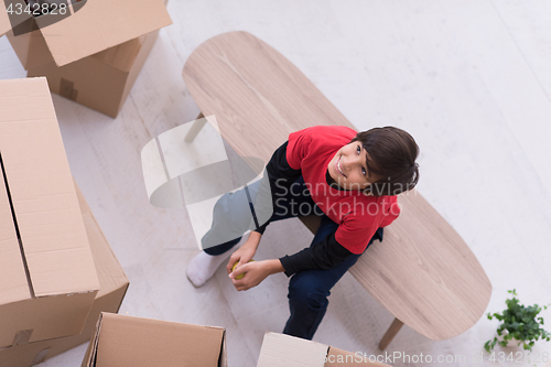 Image of boy sitting on the table with cardboard boxes around him top vie