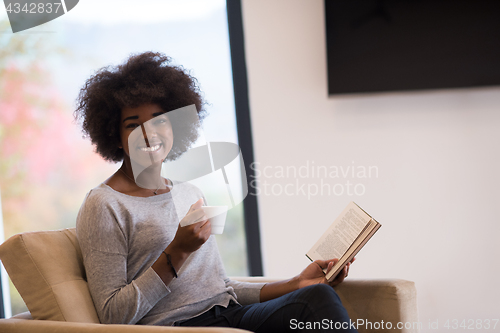 Image of black woman reading book  in front of fireplace