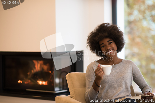 Image of black woman reading book  in front of fireplace